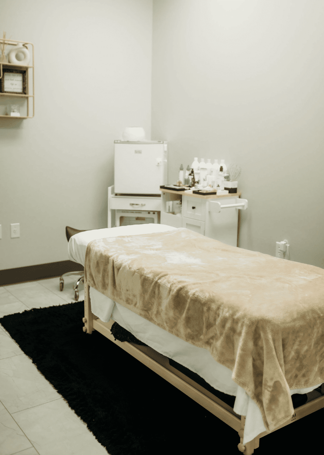 Massage therapy room with treatment table, cozy blanket, shelves, and relaxation amenities.