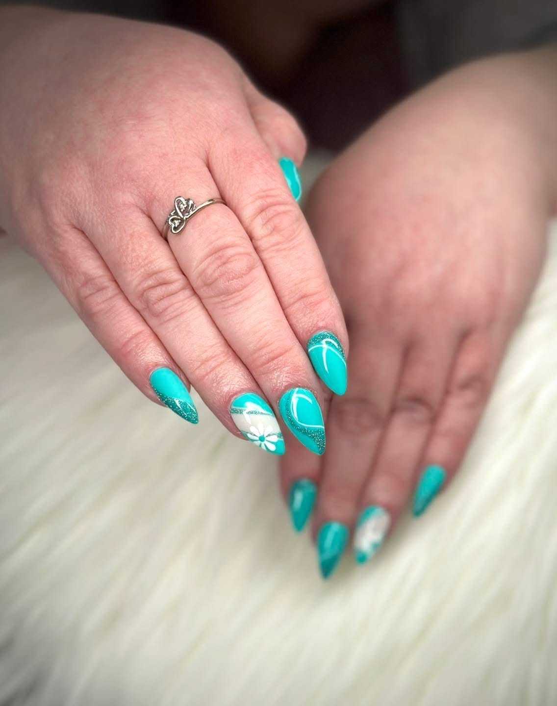 Teal nails with floral and geometric designs on a white fluffy background.