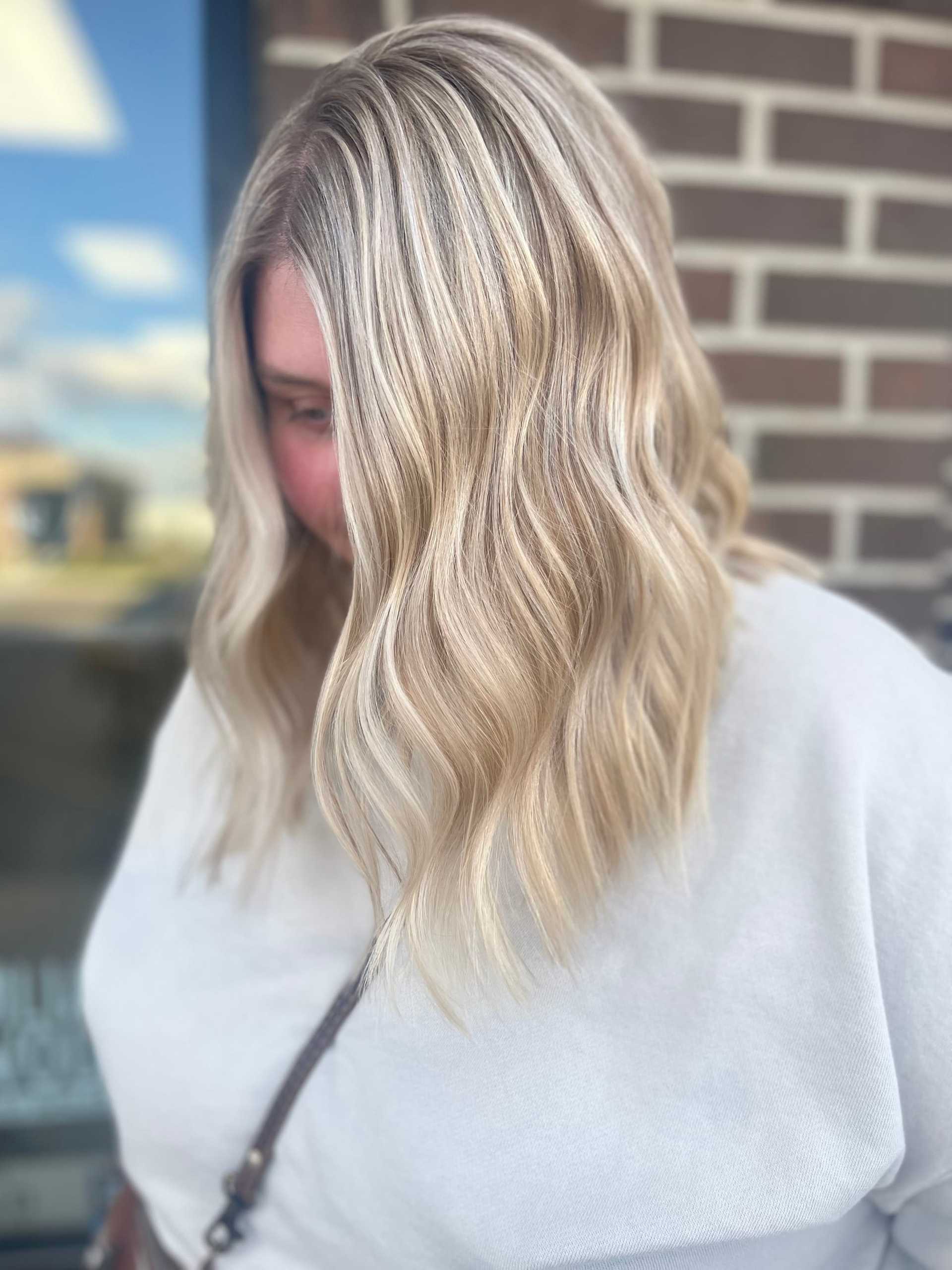 Wavy blonde hair with highlights against a brick wall background.