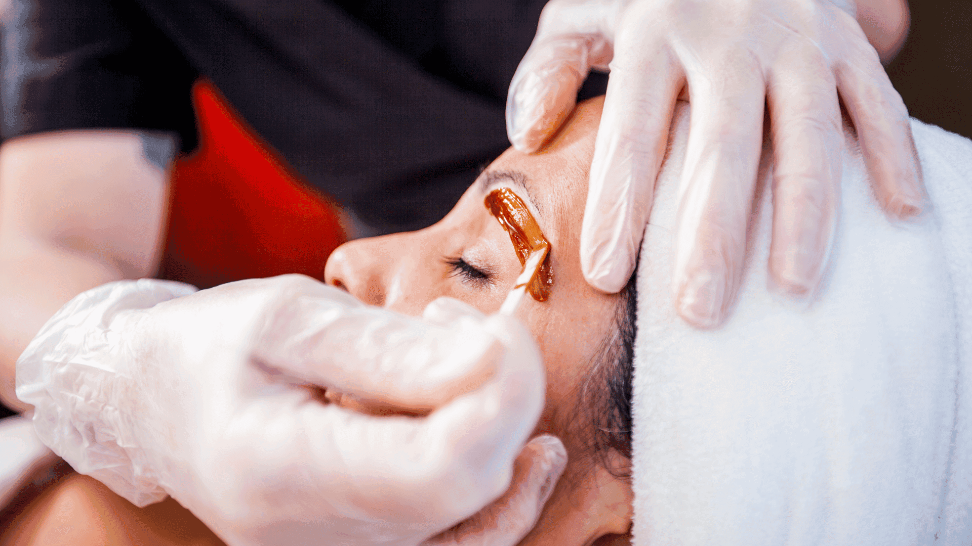 Eyebrow waxing session with stylist applying wax on a client's brow under bright lighting.