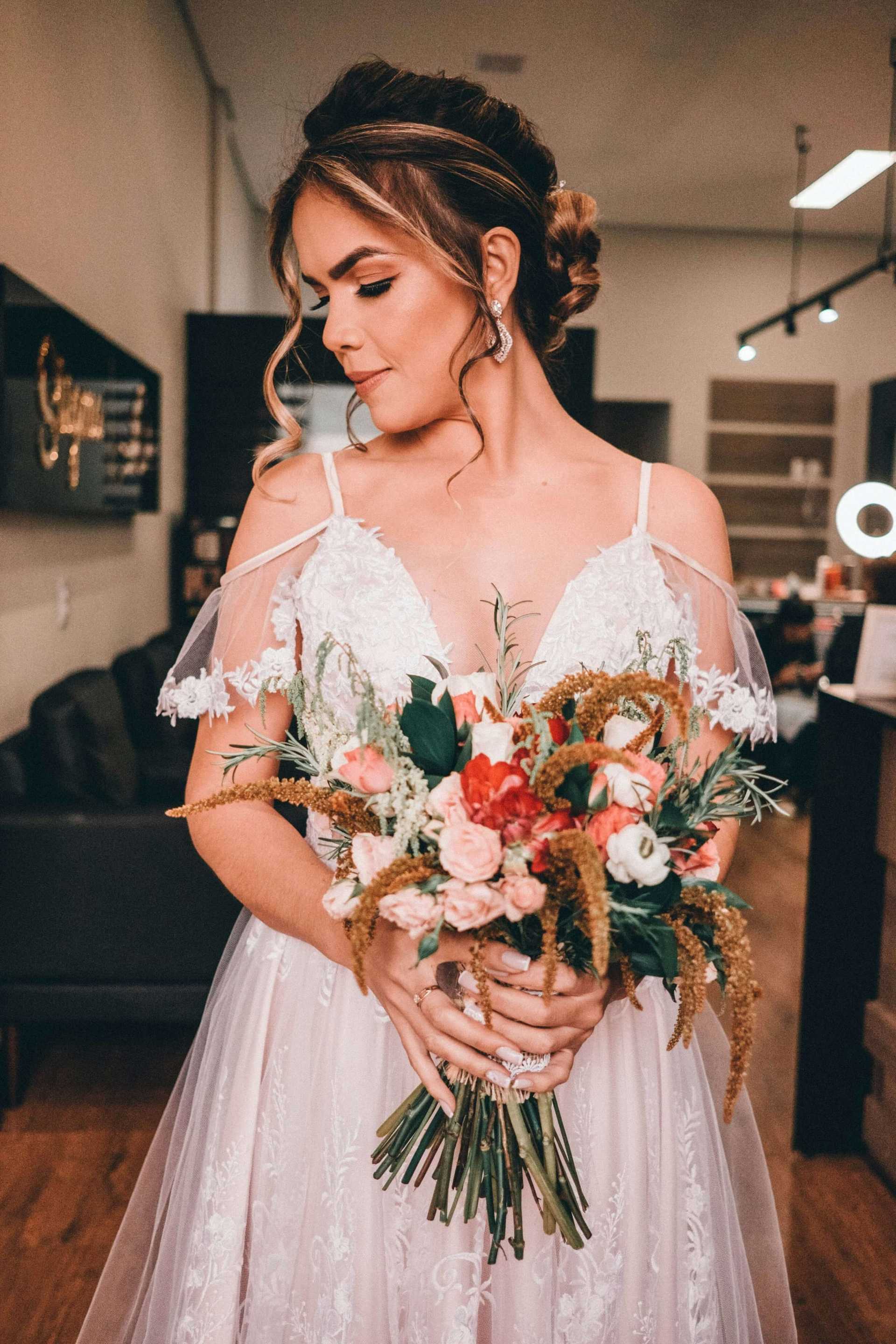 Bride holding bouquet in elegant room, looking serene in lace wedding dress.